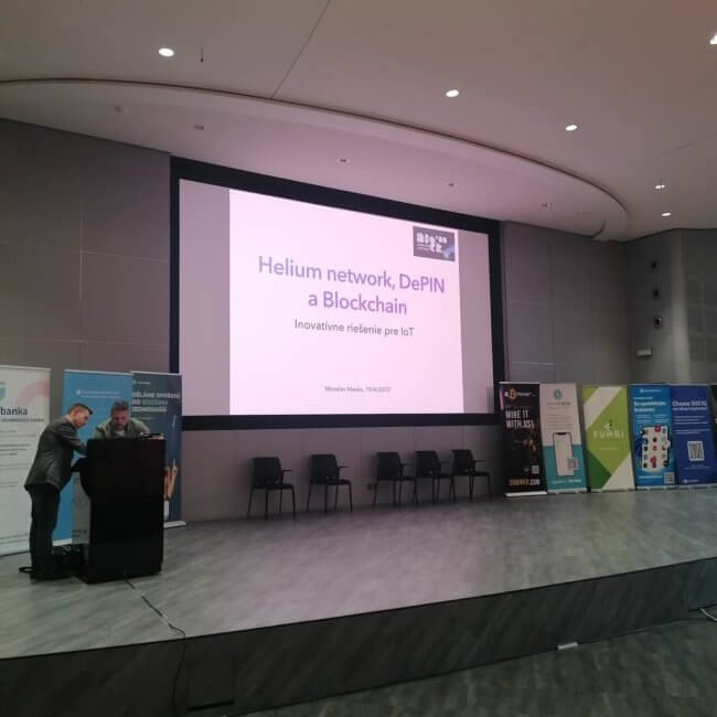Helium network DePIN blockchain presentation screen on a podium with speaker and organizer on the left