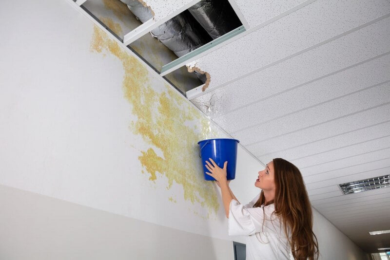 woman standing under a ceiling with bucket collecting water after water leak